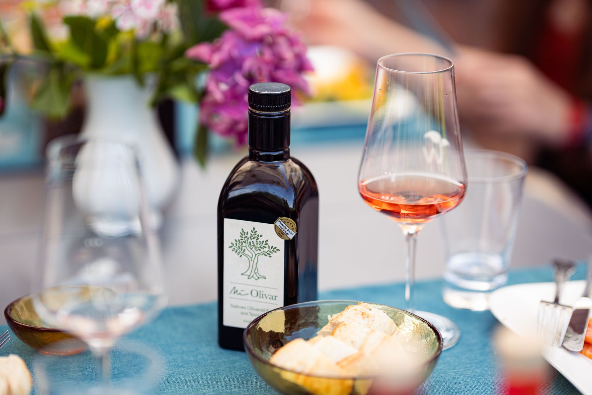 A bottle of wine, a glass of wine, and a bowl of bread on a table.