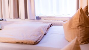 Een hotelkamer met een bed, kussens en een raam met dunne gordijnen.