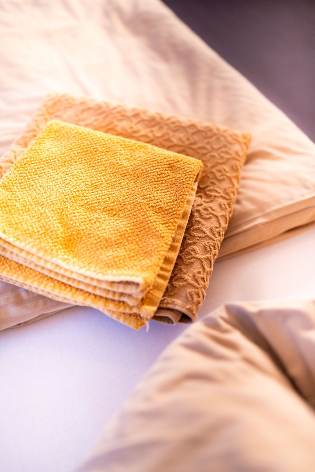 Una cama con ropa de cama color beige y una toalla amarilla doblada.