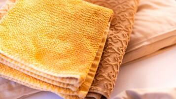 Una cama con ropa de cama color beige y una toalla amarilla doblada.