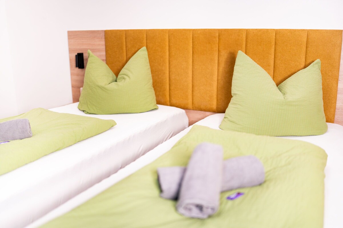 A hotel room with two beds, each with green bedding and matching pillows.