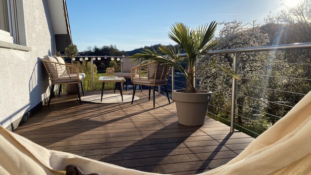 Een balkon met een hangmat, stoelen, een tafel en een potplant.