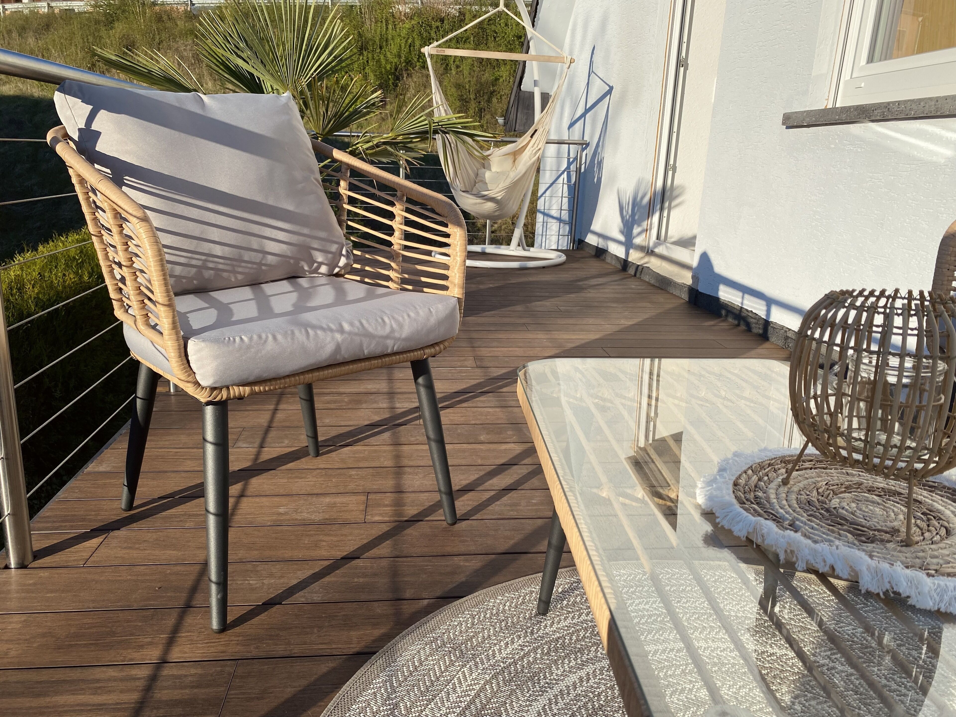 Eine Holzterrasse mit einem Korbstuhl und einem Glastisch.