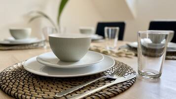 Une table à manger dressée avec des assiettes blanches, un bol, des couverts et un verre.