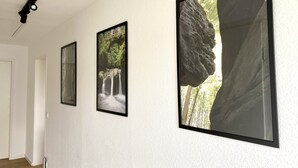 Een gang met drie ingelijste foto's aan de muur, een deur en een plafondlamp.