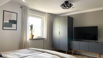 A bedroom with a bed, a TV, a wardrobe, and a window with curtains.