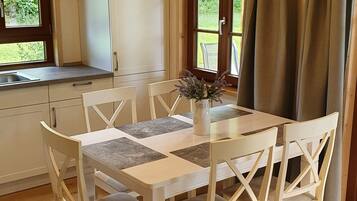 Ein Essbereich mit einem weißen Tisch und Stühlen, einer Vase mit Blumen und einem Fenster mit Vorhängen.