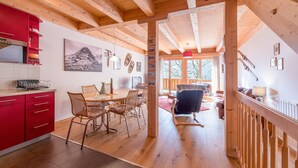 A spacious kitchen with wooden beams, a dining area with chairs, and a staircase leading to a loft.