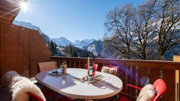 A round table with chairs on an outdoor deck, overlooking snow-capped mountains and a clear blue sky.