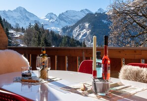 A table set outdoors with a mountain view, featuring a bottle, glasses, and a candle. - Racers Retreat 3 (Wengen)