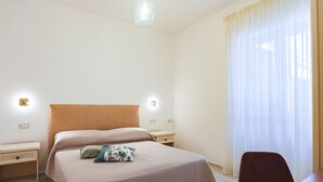 Una camera d'albergo con un letto, comodini, una scrivania con una sedia, una lampada e una finestra con tende.
