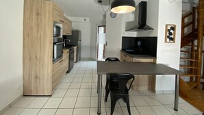 A modern kitchen with wooden cabinets, a stainless steel refrigerator, a black countertop, and a dining area with a table and chairs.