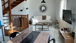 A modern living space with a wooden staircase, a sofa, a dining table, and a TV.