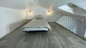 A bedroom with a sloped ceiling, a bed with a patterned bedspread, two wall-mounted lights, and a small round table.