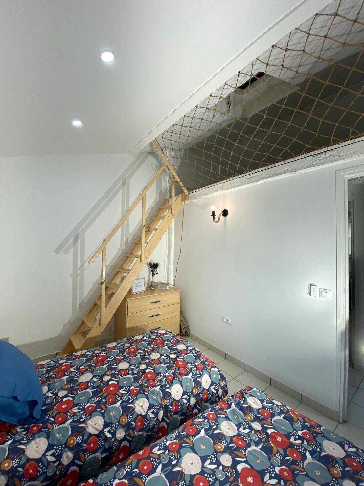 Une chambre à coucher avec un lit, un escalier en bois, une table de chevet et un luminaire fixé au mur.