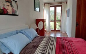 Een slaapkamer met een bed, een ventilator en uitzicht op buiten.