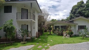 Un bâtiment à deux étages doté d’un balcon, entouré d’un jardin bien entretenu où poussent différentes espèces de plantes, et où se trouve un vélo.