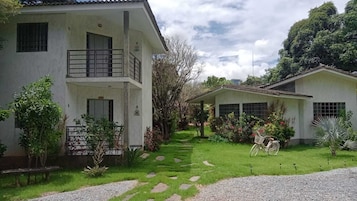 Un edificio de dos pisos con un balcón, rodeado de un jardín cuidado con diversas plantas y una bicicleta.