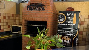 Un four à briques portant l’inscription « Cantinho Currosca », installé dans un espace extérieur abrité, avec des murs recouverts de carreaux et une plante en pot posée sur le comptoir.