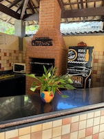 Un horno de ladrillo con la leyenda 'Cantinho Currosca' en un espacio al aire libre cubierto, con paredes de azulejos y una planta en maceta sobre el mostrador.