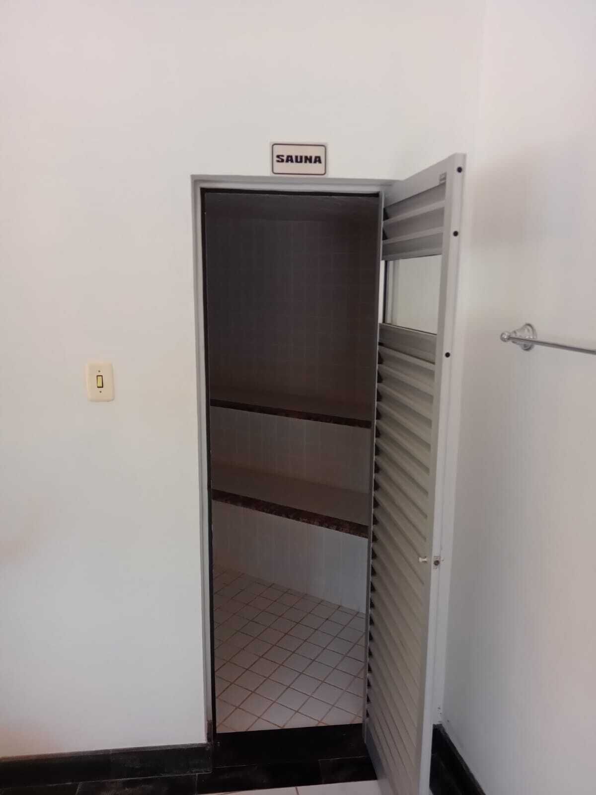 Puerta cerrada de una sauna con un cartel encima, suelo de azulejos y pared blanca.
