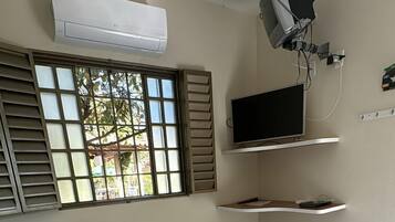 Un dormitorio con cama, televisor, aire acondicionado y ventana con persianas.