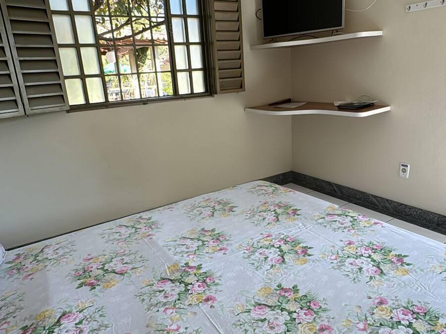 Un dormitorio con cama, televisor, aire acondicionado y ventana con persianas.