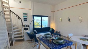 A modern kitchen with a dining area, a staircase, and a view of the sea.