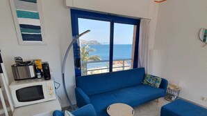 A modern living room with a blue sofa, two armchairs, a small round table, and a view of the sea.