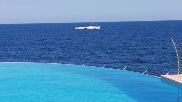 A pool with a view of the ocean and a yacht in the distance.
