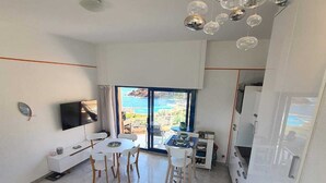 A modern living room with a dining area, a TV, and a view of the sea.