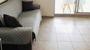 Un salón con sofá, puerta de vidrio que da a un balcón con mesa y sillas.