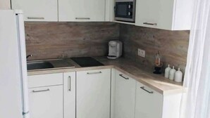 Una cocina compacta con armarios blancos, un microondas, una cafetera y un lavamanos.