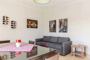 Uma sala de estar moderna com uma mesa de jantar de vidro, um sofá cinzento e duas pinturas penduradas na parede.