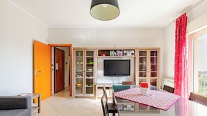 A modern living room with a glass dining table, a sofa, a TV, and built-in shelving.