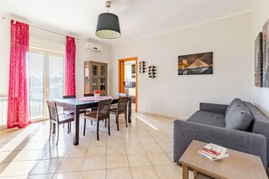 A modern living room with a dining area, a grey sofa, a table with magazines, and a painting on the wall. - SCALA DEI TURCHI APARTMENT LIDO ROSSELLO REALMONTE - CIN IT084032C26OQDV2N6 (Realmonte)