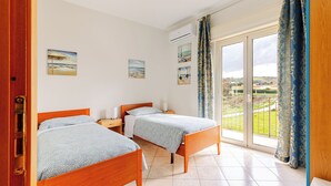 A room with two wooden beds, a window with a view, and a door.