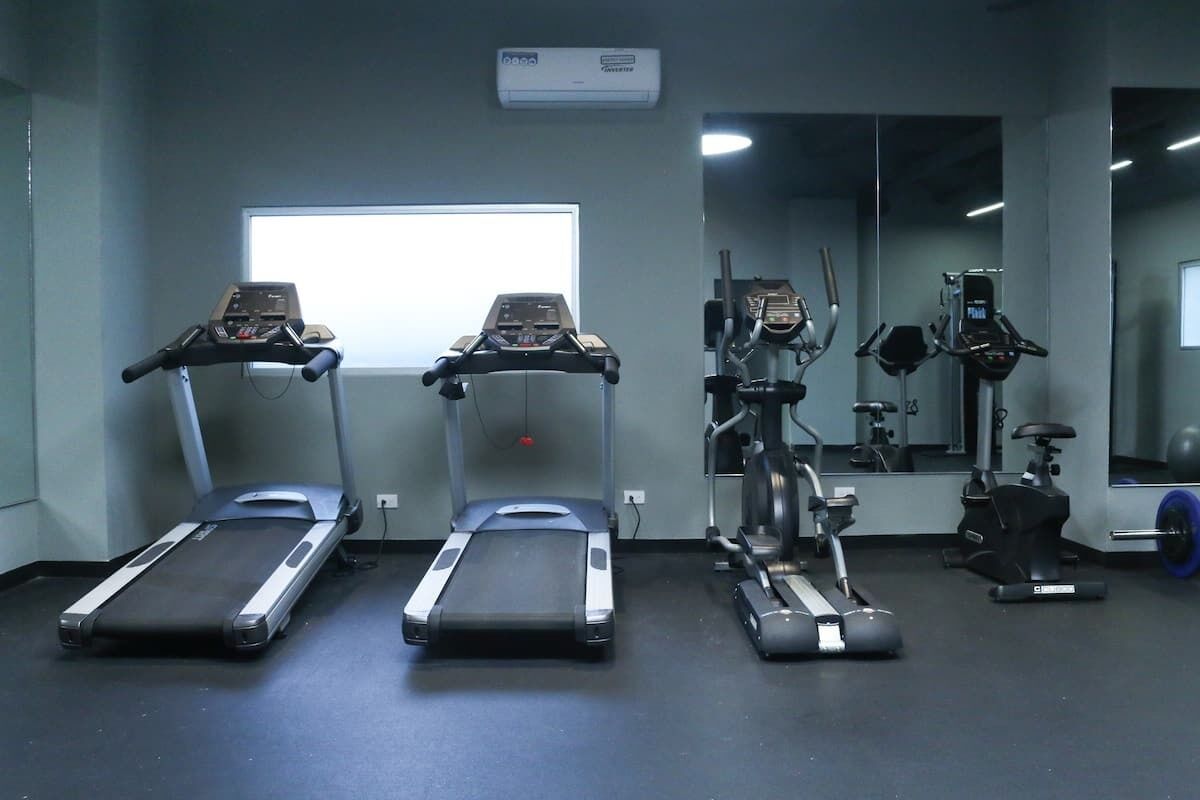 Une salle de sport équipée de tapis de course, de vélos elliptiques et d’un mur recouvert de miroirs.