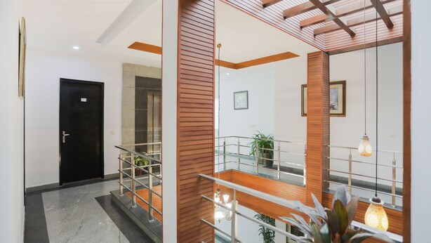 A modern hotel lobby with a staircase, wooden accents, and a view of the interior. - Dormy Villa By Dreamz Hospitality (Gurugram)