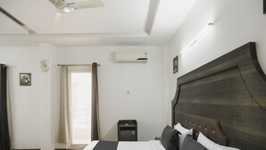 A hotel room with a large bed, a ceiling fan, an air conditioning unit, a small desk, and a window with curtains. - Dormy Villa By Dreamz Hospitality (Gurugram)