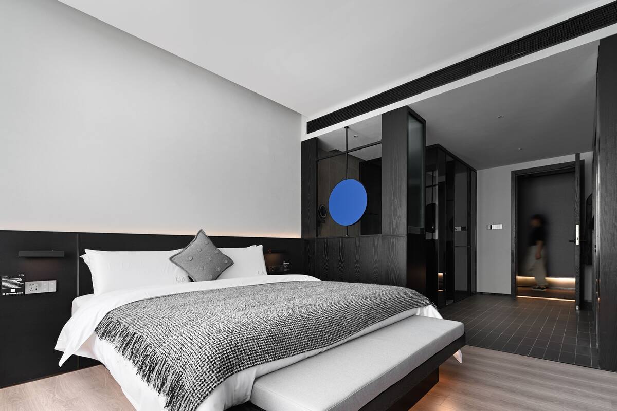 A modern hotel room with a large bed, a built-in wardrobe, and a circular blue light fixture.
