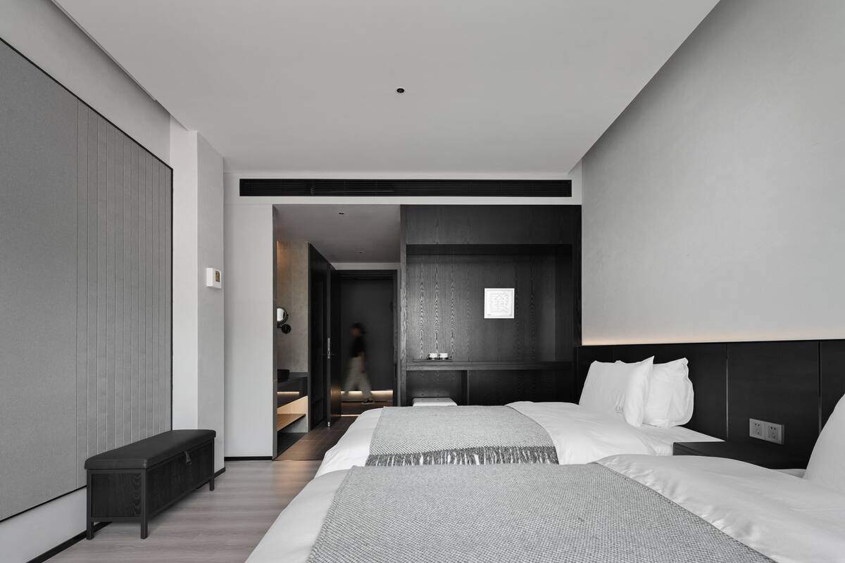 A modern hotel room with two beds, a bench, and a walk-in closet.