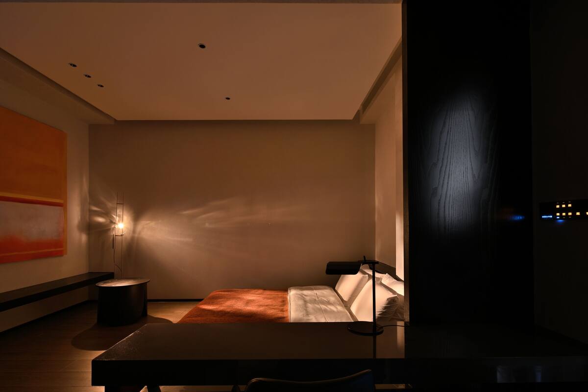 A modern hotel room with a bed, bedside table, and a wall-mounted lamp.