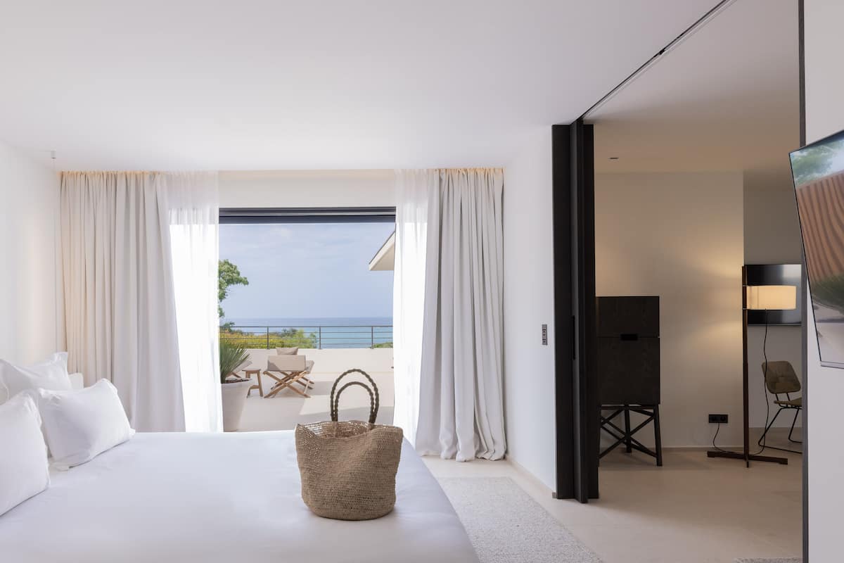 A modern hotel room with a large bed, a view of the sea, and a balcony with outdoor furniture.