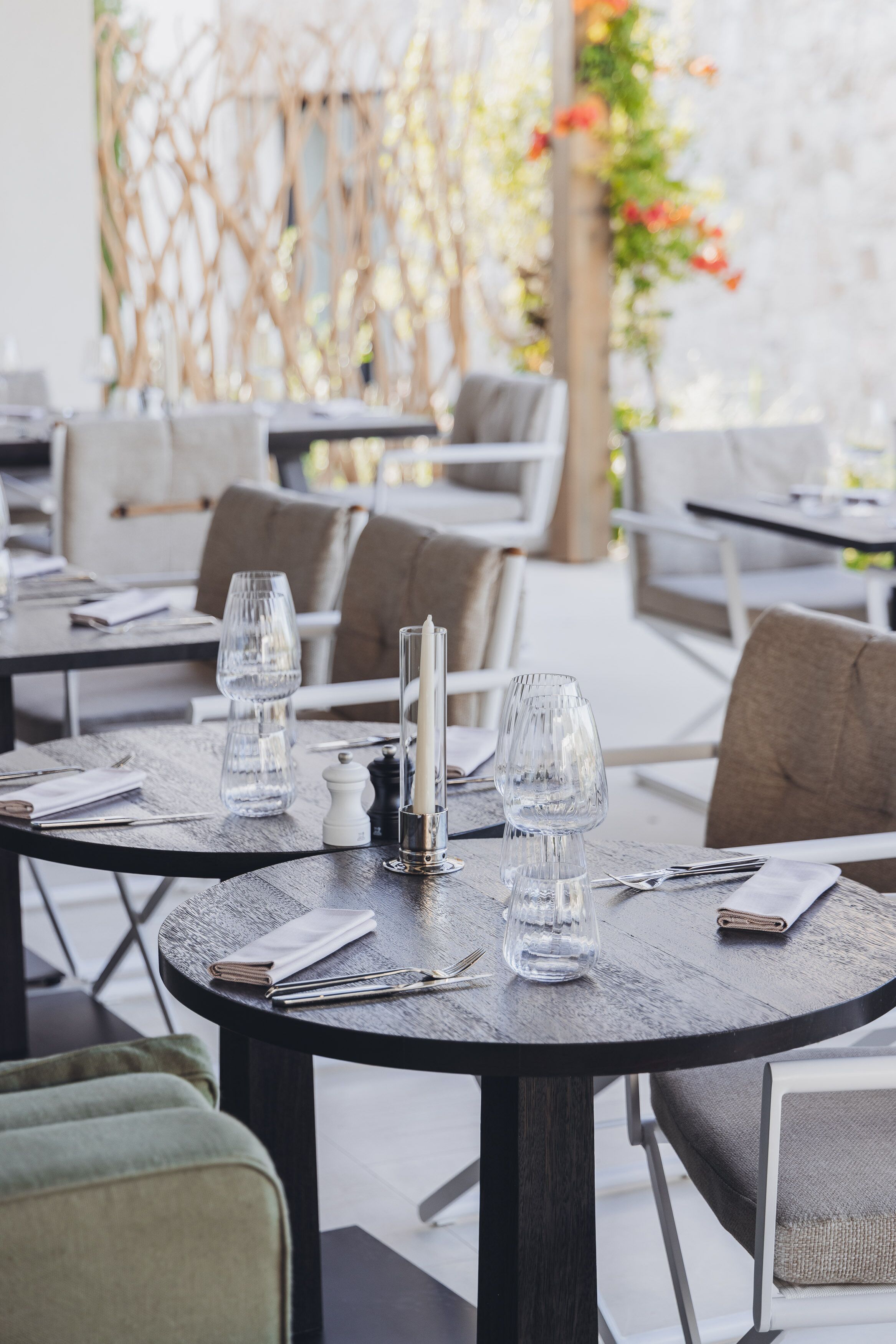 A restaurant setting with round tables, each set with a candle, glass, and cutlery.