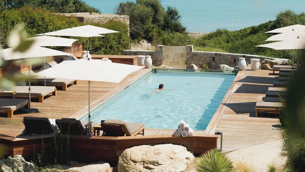 A pool area with lounge chairs and umbrellas, surrounded by greenery and overlooking the sea. - Casa Paradisu (Monticello)