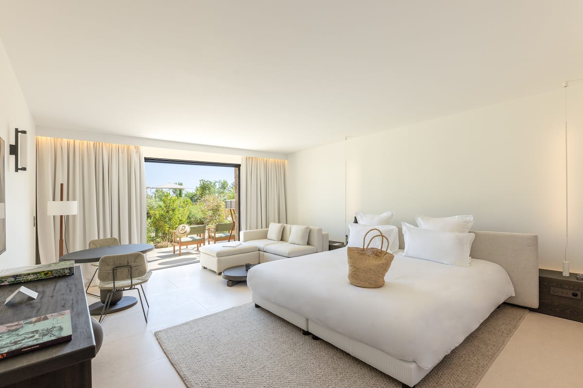 A modern hotel room with a large bed, a desk, a sofa, and a dining area.
