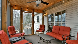 A covered porch with a ceiling fan, wooden beams, and string lights. There are several red chairs and a metal table.