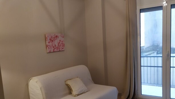 A minimalist living room with a white sofa, a small table with a remote control, and a window with curtains. - On the Metro Station of Korydallos, Near Peiraeus (Korydallos)