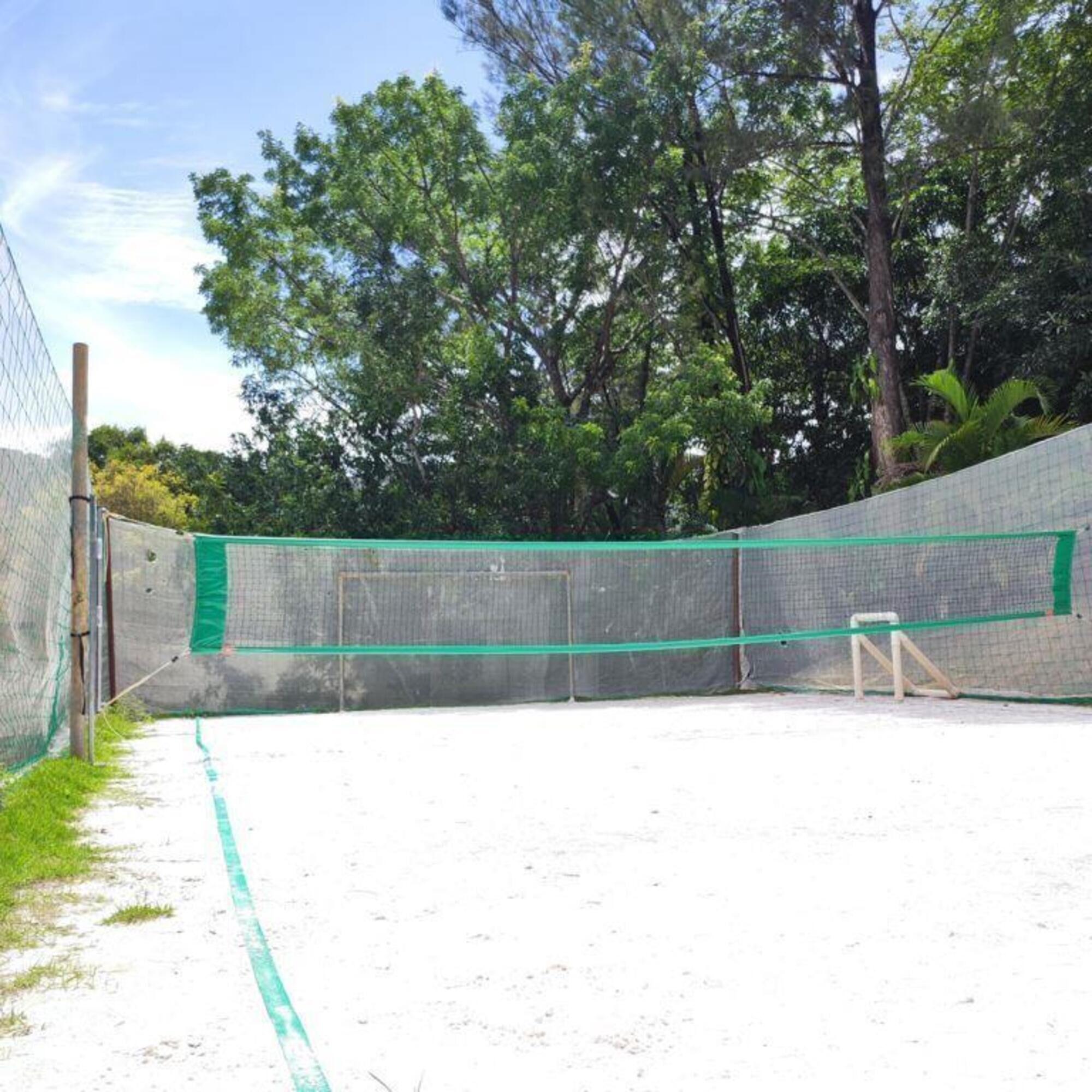 A tennis court with a net, surrounded by a fence and trees.